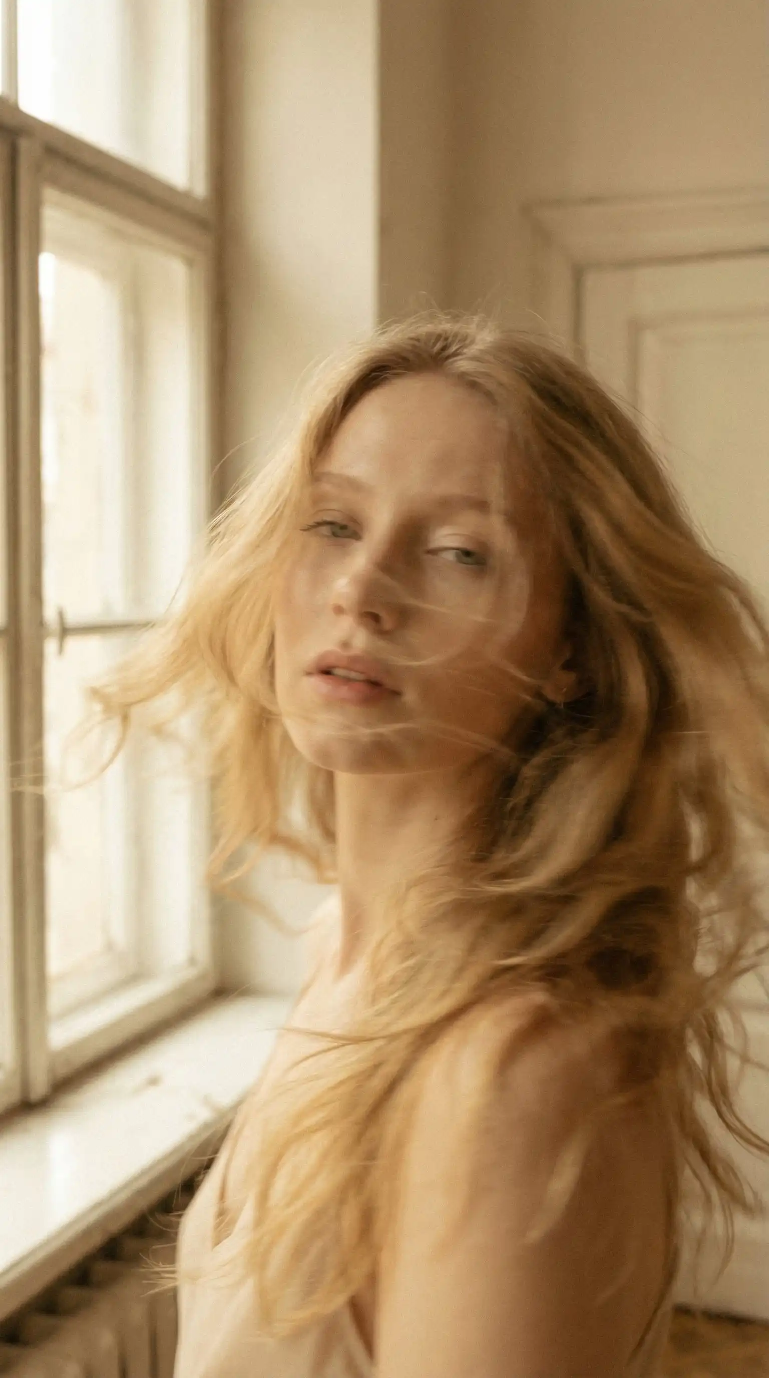 trend prompt: Soft cinematic portrait of a young woman with light golden hair in motion. Slight blur and ghost effect, hair flowing, dreamy look. Calm expression, soft eyes, parted lips. Warm golden