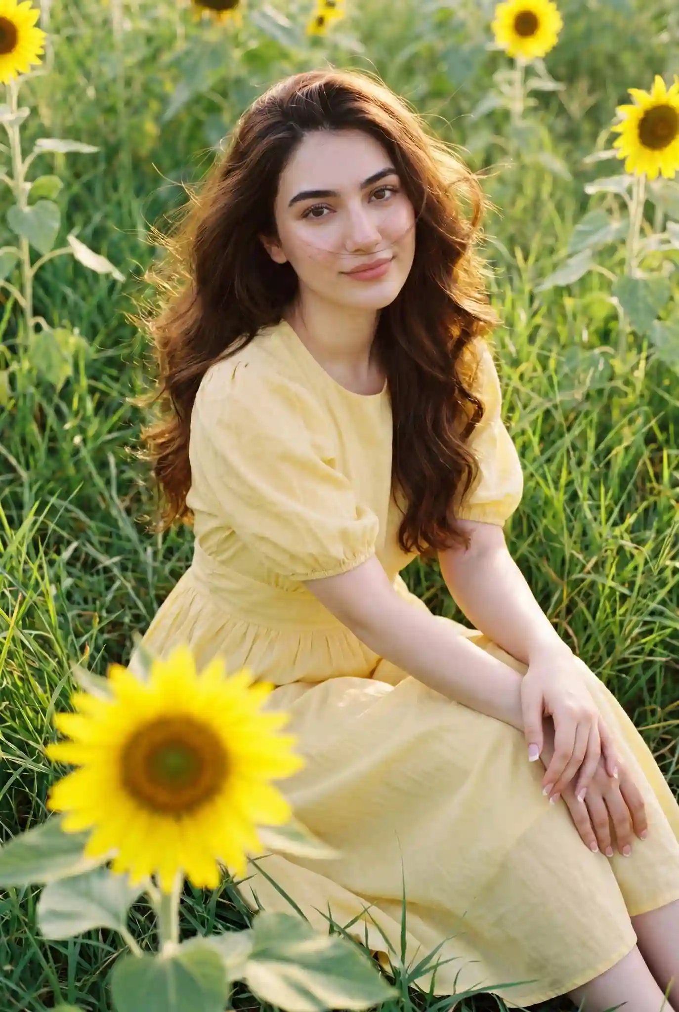 trend prompt: A girl is sitting in tall green grass among sunflowers. She is wearing a soft yellow, feminine midi dress with puff sleeves, a fitted waist, and a flowy skirt. The dress has a delicate, romantic style. She is looking at the camera, with the same emotions as in the original image.
In the foreground, slightly to the side, a sunflower is partially visible and blurred (out of focus) to create a sense of depth and motion.
Her hair is long, voluminous, and shiny, gently blowing in the wind, with some strands falling across her face.
Cinematic look with subtle film grain.
French manicure nails.
Skin appears smooth, glowing, and softly illuminated.