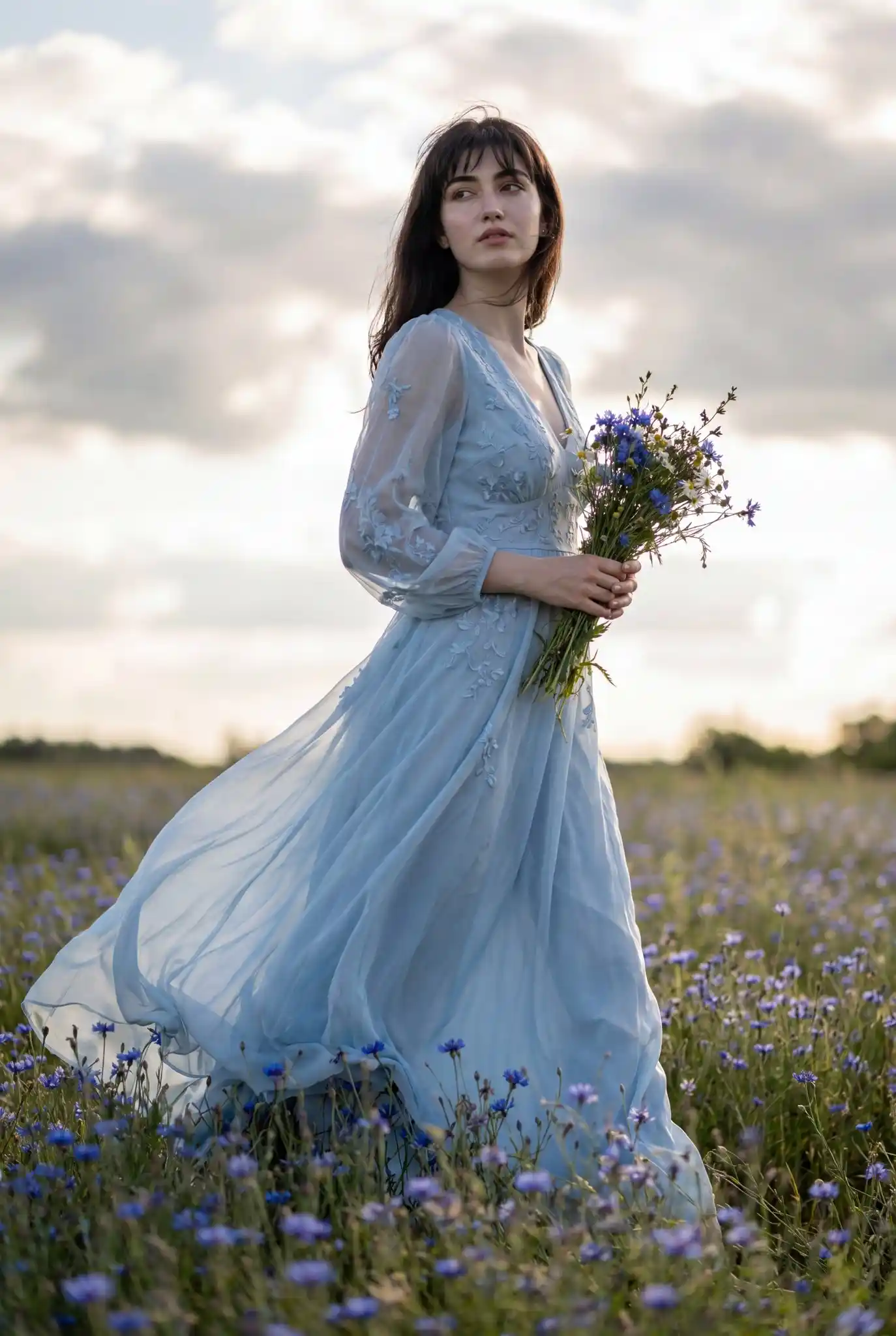 trend prompt: Ultra-realistic full-body fashion portrait of her with long dark brown hair and soft wispy bangs, walking through a vast field of blooming blue wildflowers under natural daylight. She is captured from a slightly low-angle perspective, creating a cinematic editorial feel. She wears an elegant flowing light-blue chiffon gown with delicate embroidery, sheer billowing sleeves, subtle lace detailing, and realistic fabric movement from a gentle breeze. The dress has a tasteful thigh slit and layered translucent textures that catch the sunlight naturally.
She holds a fresh handpicked bundle of vivid blue wildflowers close to her chest while walking gracefully through the meadow. Her makeup is soft and refined with natural glowing skin, subtle peach blush, feathered brows, soft brown eyeliner, glossy muted rose lips, and realistic skin texture with visible pores and fine facial detail. Her expression is dreamy and contemplative, looking slightly away from the camera.
Golden sunlight filters through scattered clouds in a bright blue sky, creating realistic highlights and soft shadows across her face, hair, and dress. The wind gently lifts strands of hair and flowing fabric. Foreground flowers are softly blurred with realistic depth of field, while distant wildflowers fade naturally into the background. Cinematic photography, ultra-detailed realism, luxury fashion editorial aesthetic, realistic anatomy, realistic hands, natural proportions, HDR photography, shallow depth of field, shot on a full-frame mirrorless camera, 85mm lens, f/1.8, high dynamic range, photorealistic textures, soft atmospheric lighting, Vogue-style outdoor editorial shoot, no fantasy elements, no CGI look, no anime style.