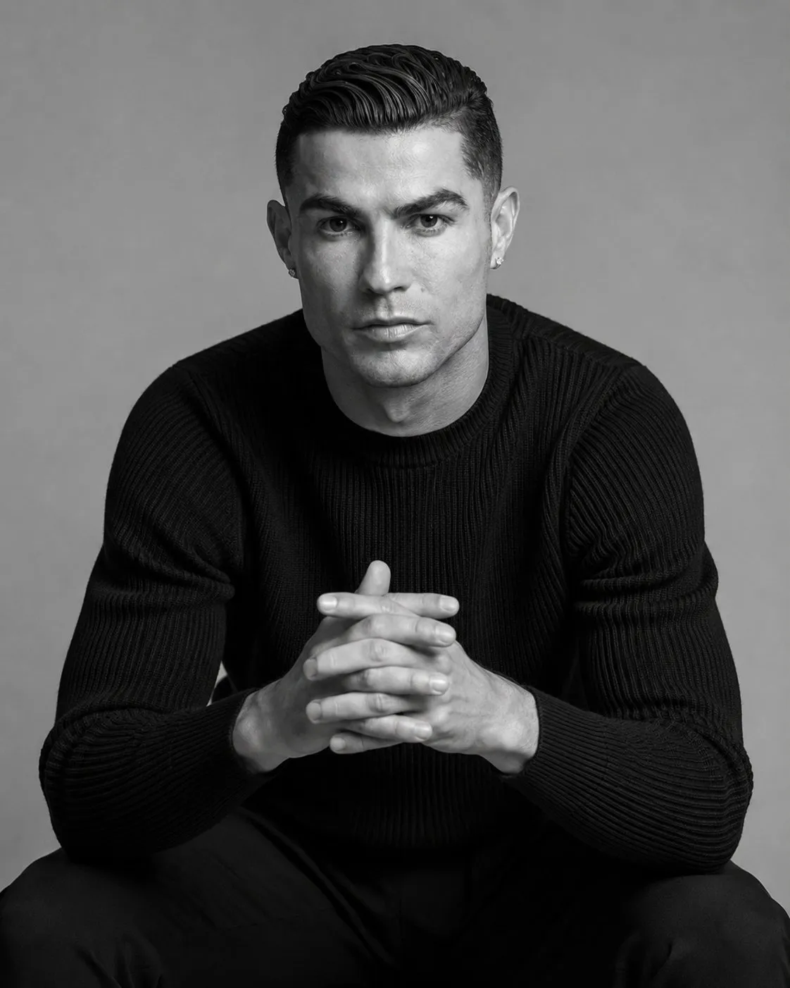 trend prompt: Use the uploaded photo only for facial identity and overall appearance. Create a premium black-and-white studio portrait of the same person seated slightly forward toward the camera in a confident yet relaxed pose. Elbows resting on the knees, hands loosely clasped together, creating natural depth and a strong editorial presence. The subject wears a fitted black ribbed knit sweater with a clean luxury aesthetic. Direct eye contact with the camera, calm yet intense expression, strong jawline, defined facial features, natural skin texture, and a confident masculine presence. Hair is neatly styled with a clean fade on the sides and textured volume on top. Small diamond stud earrings in both ears. Photographed at eye level with an 85mm portrait lens for a premium fashion-editorial look. Soft studio lighting from the front and slightly from the side creates gentle shadows and realistic facial definition without harsh contrast. Seamless light-gray studio backdrop with a subtle gradient, completely clean and distraction-free. High-end fashion campaign aesthetic, luxury magazine portrait, timeless monochrome tones, ultra-realistic details, cinematic depth, premium retouching, sharp focus on the eyes, elegant composition, professional studio photography, 8K ultra-realism, 4:5 aspect ratio.