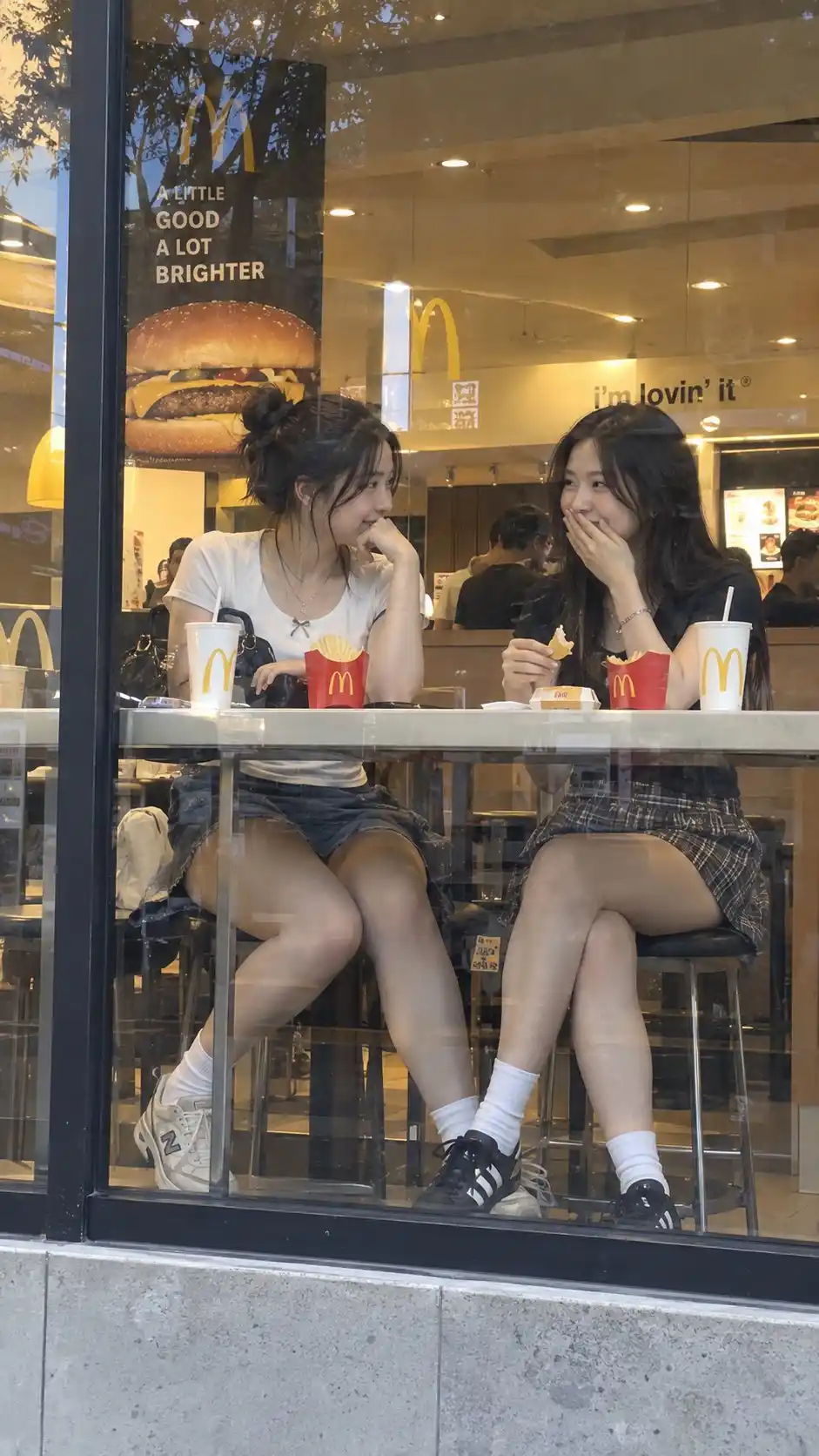 trend prompt: Bro this McDonald's looks suspiciously perfect GPT image 2 prompt : Ultra-realistic candid 9:16 street photograph of two adult East Asian women in stylish short skirts, sitting casually at a window-side counter inside McDonald's, naturally chatting together. Photographed from the sidewalk through the glass window, with realistic reflections, warm interior lighting, natural body language, authentic expressions, detailed skin and clothing textures, shallow depth of field, and an unposed smartphone photography feel