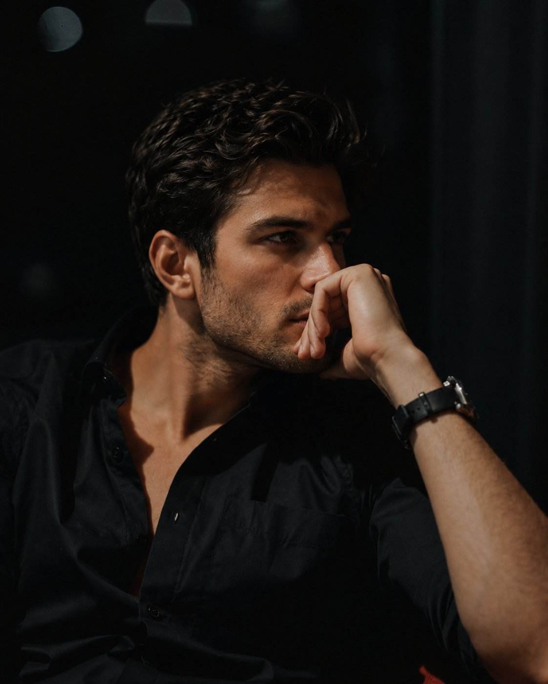 GPT Image 2 prompt: Ultra-realistic cinematic portrait of a handsome young man sitting alone at night in a dimly lit luxury lounge or café, wearing a fitted black button-up shirt with the top buttons open and a black leather wristwatch. He rests his chin on his hand in a thoughtful pose, gazing out of frame with an intense, contemplative expression. Warm cinematic side lighting illuminates one side of his face, creating dramatic shadows and emphasizing sharp facial features, textured stubble, and styled wavy dark hair. Dark moody background with soft bokeh lights and reflections on glass, deep blacks, subtle amber highlights, shallow depth of field, professional photography, luxury editorial aesthetic, emotional storytelling, ultra-detailed skin texture, realistic lighting, high contrast, premium fashion magazine style, shot on an 85mm lens, f/1.4, photorealistic, 8K, masterpiece quality.

Negative Prompt:
blurry, low quality, cartoon, CGI, overexposed, oversaturated, extra fingers, distorted face, bad anatomy, duplicate features, smiling, looking at camera, bright daylight, cluttered background, low resolution, noise, watermark, text, logo, artificial skin, unrealistic lighting.

Lighting: Warm cinematic side light
Style: Luxury editorial, moody, photorealistic
Quality: Ultra-detailed 8K, HDR, shallow depth of field.