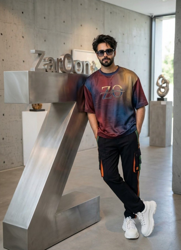 vip prompts: A hyper-realistic, high-fashion photograph of a stylish young man in a modern industrial art gallery. The man has thick, messy dark hair styled in a voluminous quiff, a full groomed beard, and is wearing dark-tinted sunglasses. He is leaning casually against a massive, brushed-steel sculpture shaped like the letter 'Z'. Perched on top of the 'Z' structure are 3D metal letters spelling out "ZarOon".
The man is dressed in trendy streetwear: an oversized t-shirt with a red, blue, and gold gradient tie-dye pattern featuring a "ZO" logo on the chest, paired with black cargo pants featuring orange and green vertical stripes on the pockets, and chunky white sneakers. He has his hands in his pockets and one leg crossed over the other.
The background is a minimalist gallery space with raw concrete walls (brutalist style) and polished concrete floors. Natural light streams in from a window on the right, creating soft shadows. In the background, there is another abstract twisted metal sculpture on a pedestal. 8k resolution, cinematic lighting, sharp focus, streetwear lookbook aesthetic.